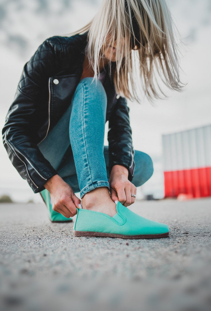 Person wearing turquoise Javer shoes and blue jeans, tying a shoe outdoors.